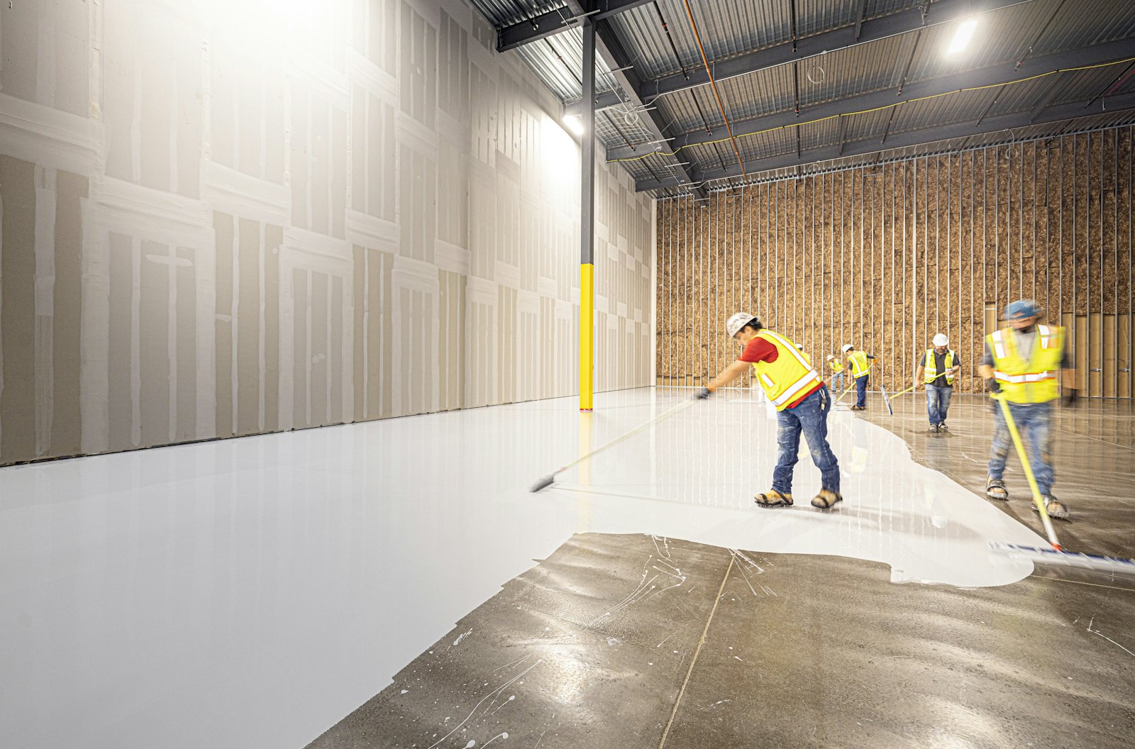 Crew applying a floor coating across a large industrial space