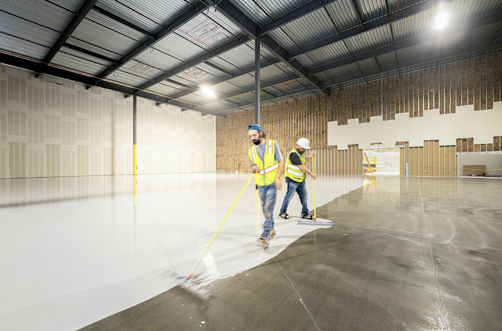 Workers coating the floor of a large empty warehouse